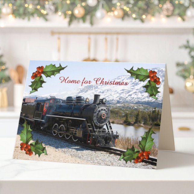 Zuhause auf dem Zug für Weihnachtskarte Feiertagskarte (A folded Christmas card of an old steam train, snowy mountains and corner decorations of holly.)