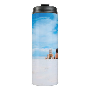 Zwei Frauen liegen auf weißem Sand und liegen dire Thermosbecher